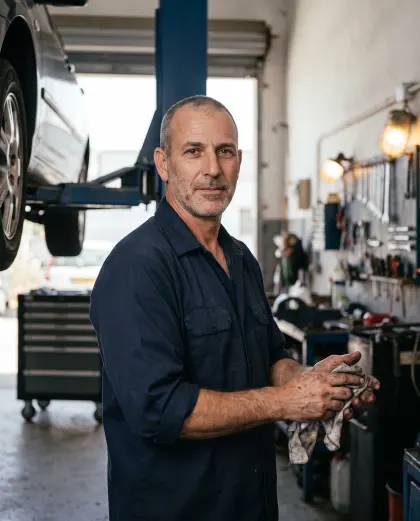 בעל מוסך עצמאי ליד רכב על מגבה, מנגב את הידיים